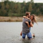 man hugging laughing woman while standing in body of water