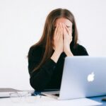 woman with hands on her face in front of a laptop