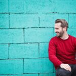 man wearing red sweatshirt and black pants leaning on the wall