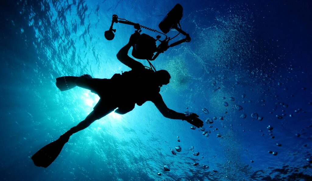 silhouette of person holding camera in body of water