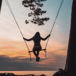 silhouette of person sitting on swing during sunset