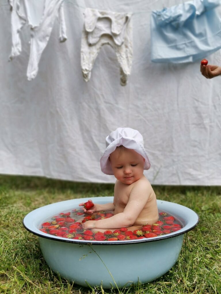 a baby bathing in a basin filled with strawberries
