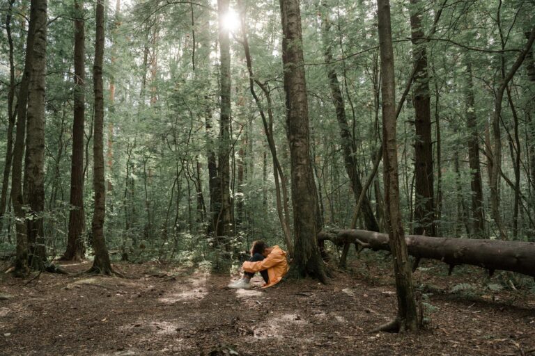a kid in yellow jacket sitting under a tree in the woods